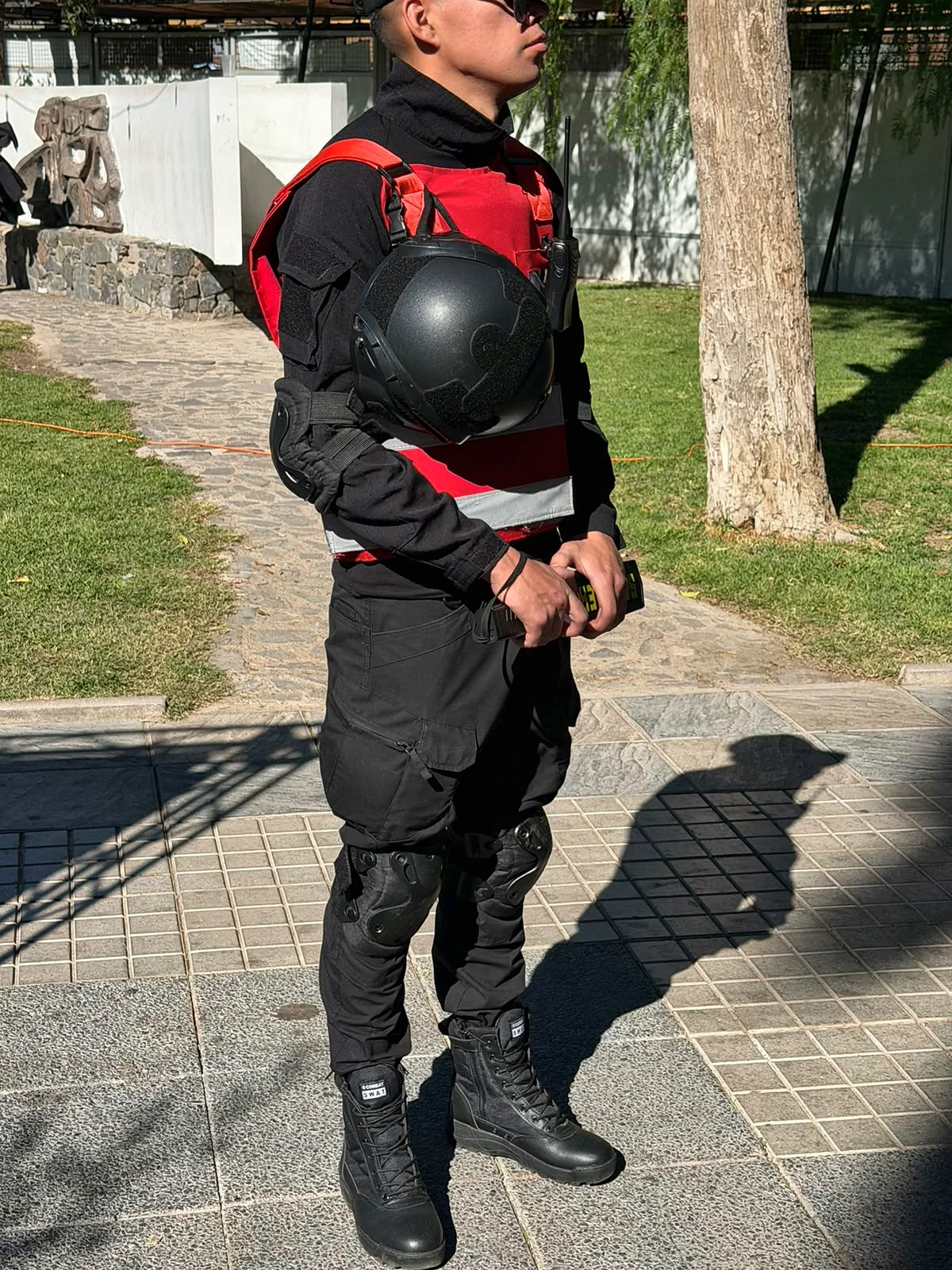 Guardia de seguridad vestido de negro con protección corporal y casco en un jardín