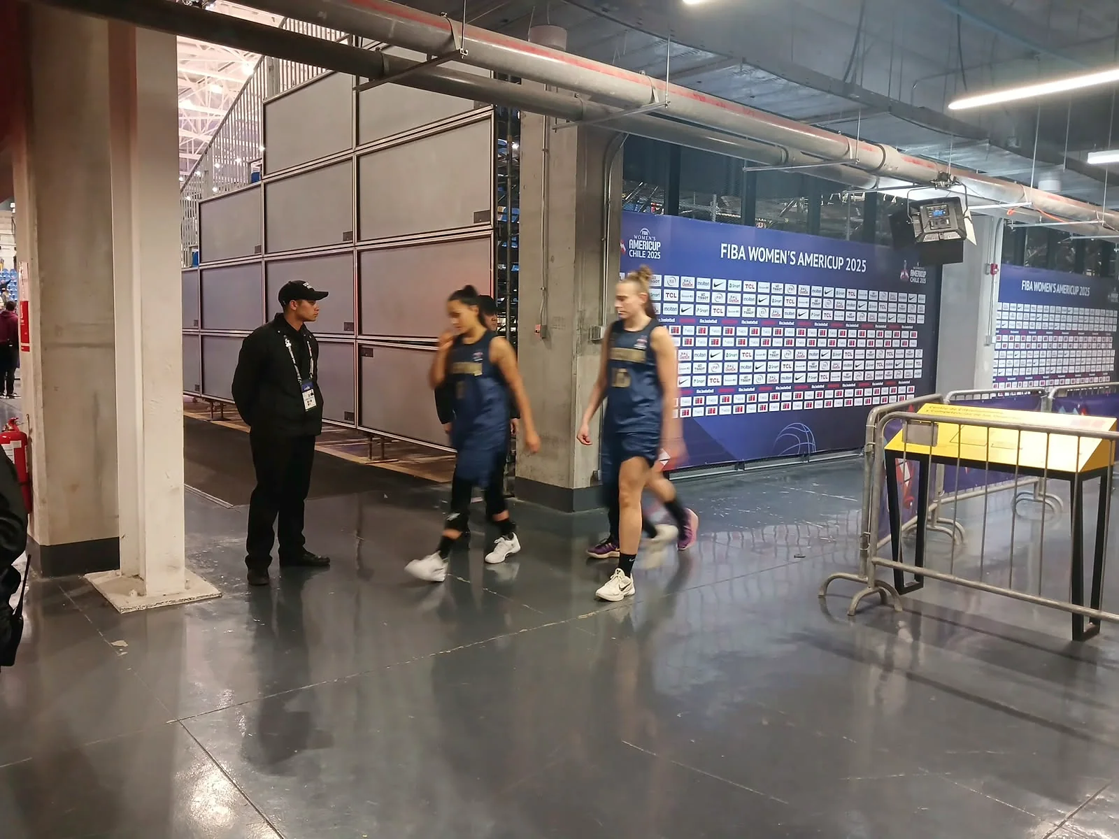 Guardia junto a deportistas en un pasillo de recinto de básquetbol