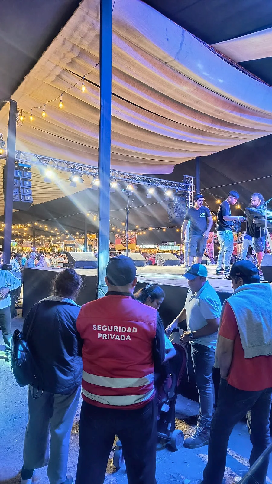 Guardia con chaleco rojo junto a escenario iluminado de un evento nocturno