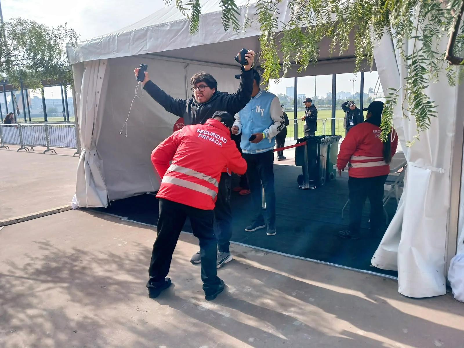 Guardia con chaqueta roja efectuando revisión a un asistente en entrada de carpa