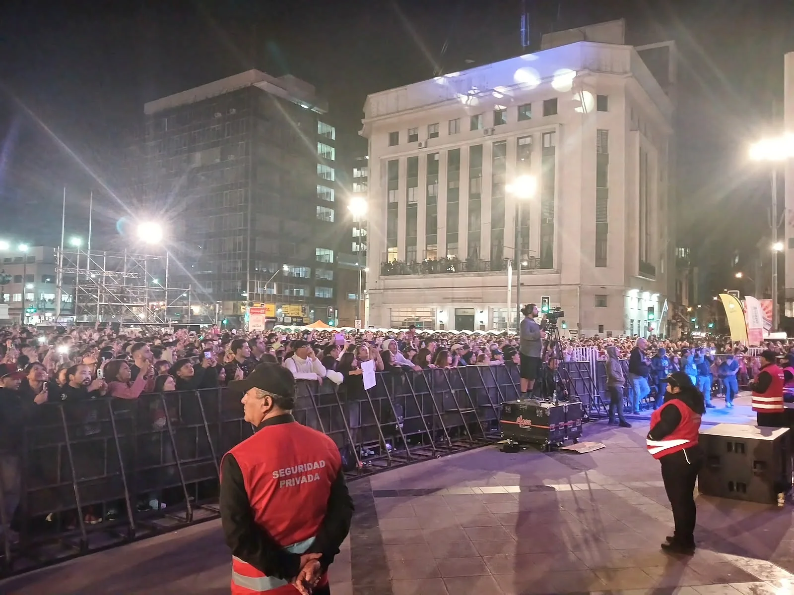 Personal de seguridad con chalecos rojos frente a multitud y vallas en ciudad